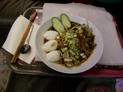 [A white bowl full of ramen soup, topped with egg, courgette, pork rind and scallionsa.]